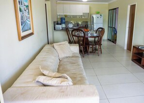 Een woonkamer met een bank, een eettafel, stoelen en een keuken op de achtergrond.
