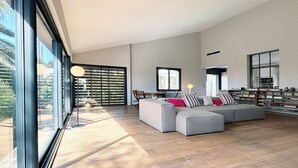 Una sala de estar amplia con un sofá modular grande, un comedor con mesa y sillas, y una estantería llena de libros.