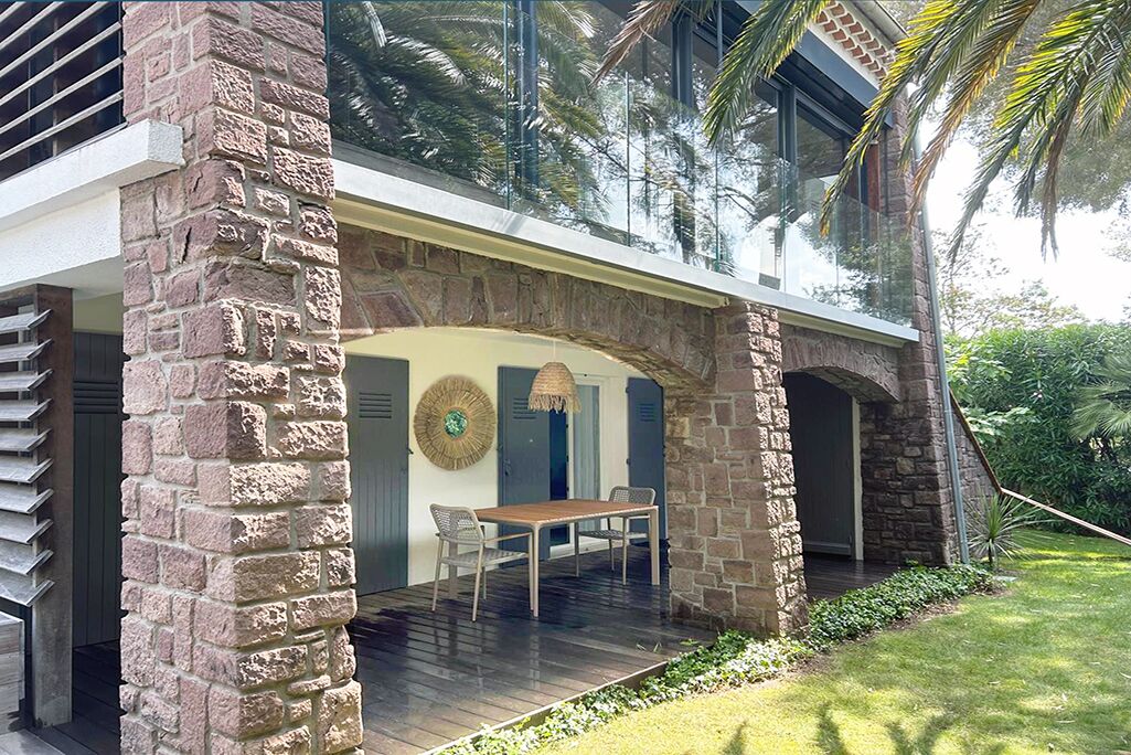 A modern house with a stone facade, a wooden deck, and a dining area with a table and chairs.