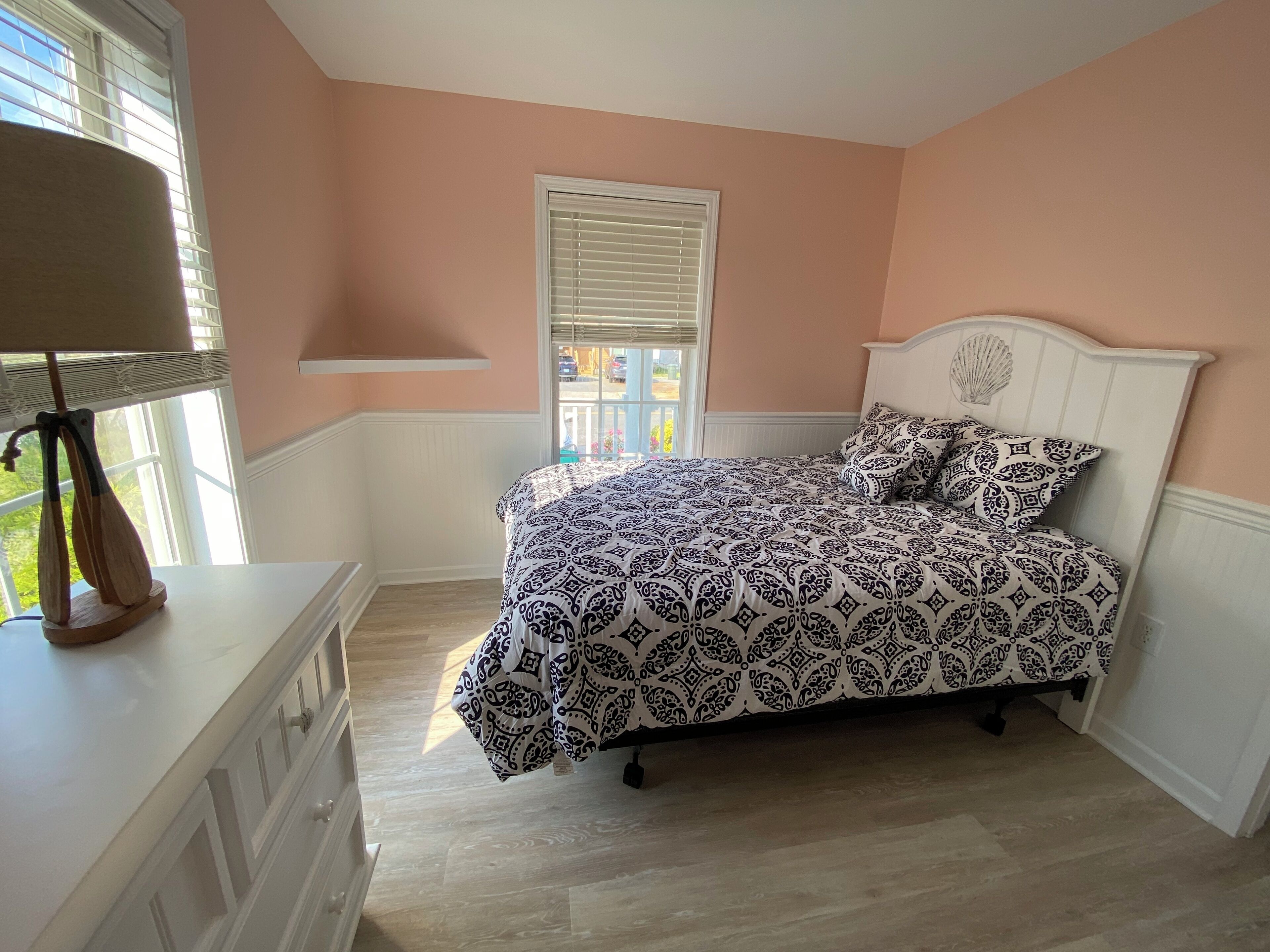 A bedroom with a bed, a dresser, a lamp, and a window with blinds.