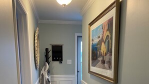Um corredor com piso de madeira, um quadro emoldurado na parede e um cabideiro com roupas penduradas.