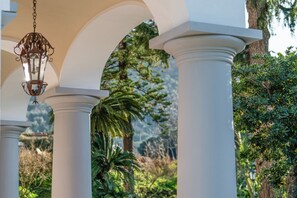 Une structure aux colonnes blanches, surmontée d’une lanterne suspendue, et entourée de verdure et d’arbres.