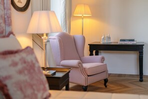 A room with a striped armchair, a side table, a lamp, and a small table with books and decorative items. - Signature Villa Overlooking the Gulf of Naples with biolake and garden (Vico Equense)