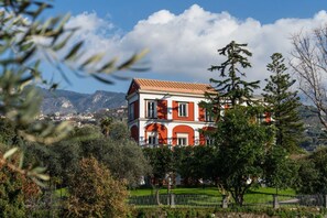 Un bâtiment à deux étages, doté d’une façade rouge et blanche, entouré de verdure et avec des montagnes en arrière-plan.