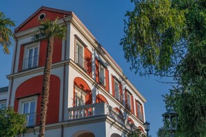 A multi-story building with a red and white facade, balconies, and arched windows. - Signature Villa Overlooking the Gulf of Naples with biolake and garden (Vico Equense)