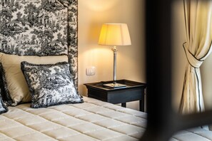 A neatly made bed with a quilted headboard, a bedside table with a lamp, and a patterned tapestry on the wall. - Signature Villa Overlooking the Gulf of Naples with biolake and garden (Vico Equense)