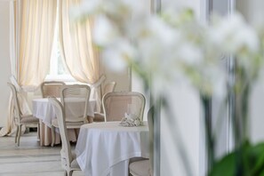 A dining area with white tablecloths, wicker chairs, and a vase of white flowers. - Signature Villa Overlooking the Gulf of Naples with biolake and garden (Vico Equense)