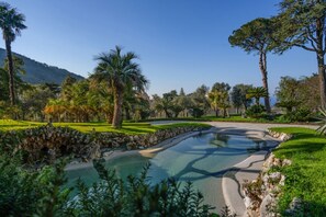 A landscaped area with a pond, stone bridge, and palm trees. - Signature Villa Overlooking the Gulf of Naples with biolake and garden (Vico Equense)