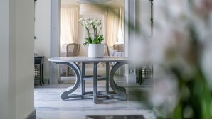 Ein Essbereich mit Tisch und Stühlen, einem Blumentopf und Blick in einen Raum mit Bett und Vorhängen.