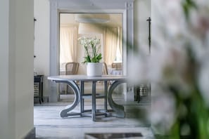 Ein Essbereich mit Tisch und Stühlen, einem Blumentopf und Blick in einen Raum mit Bett und Vorhängen.