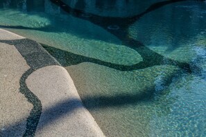 Una piscina con agua cristalina, borde de guijarros y un camino de piedra que lleva al agua.
