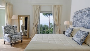 Ein Schlafzimmer mit einem großen Bett, einem Sessel, einem Spiegel und einem Balkon mit Vorhängen.
