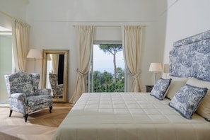 Ein Schlafzimmer mit einem großen Bett, einem Sessel, einem Spiegel und einem Balkon mit Vorhängen.