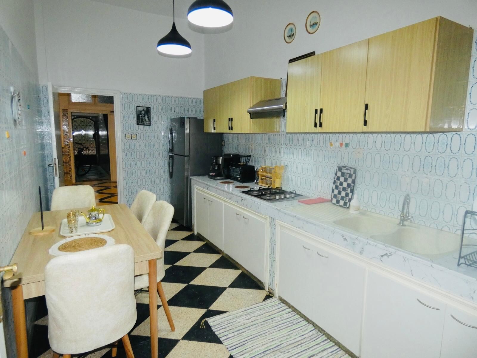 Une cuisine de taille réduite avec un carrelage à motifs, une table à manger avec des chaises, un réfrigérateur, une cuisinière et des placards en bois.