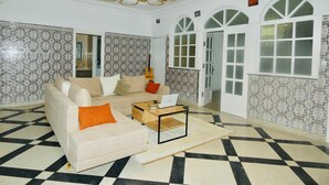 Een ruime lobby met een zwart-wit geruite vloer, een beige bank met oranje kussens, een klein houten bijzettafeltje en een kroonluchter.
