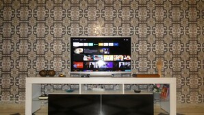 Een televisie op een witte tv-meubel met behang met een patroon.