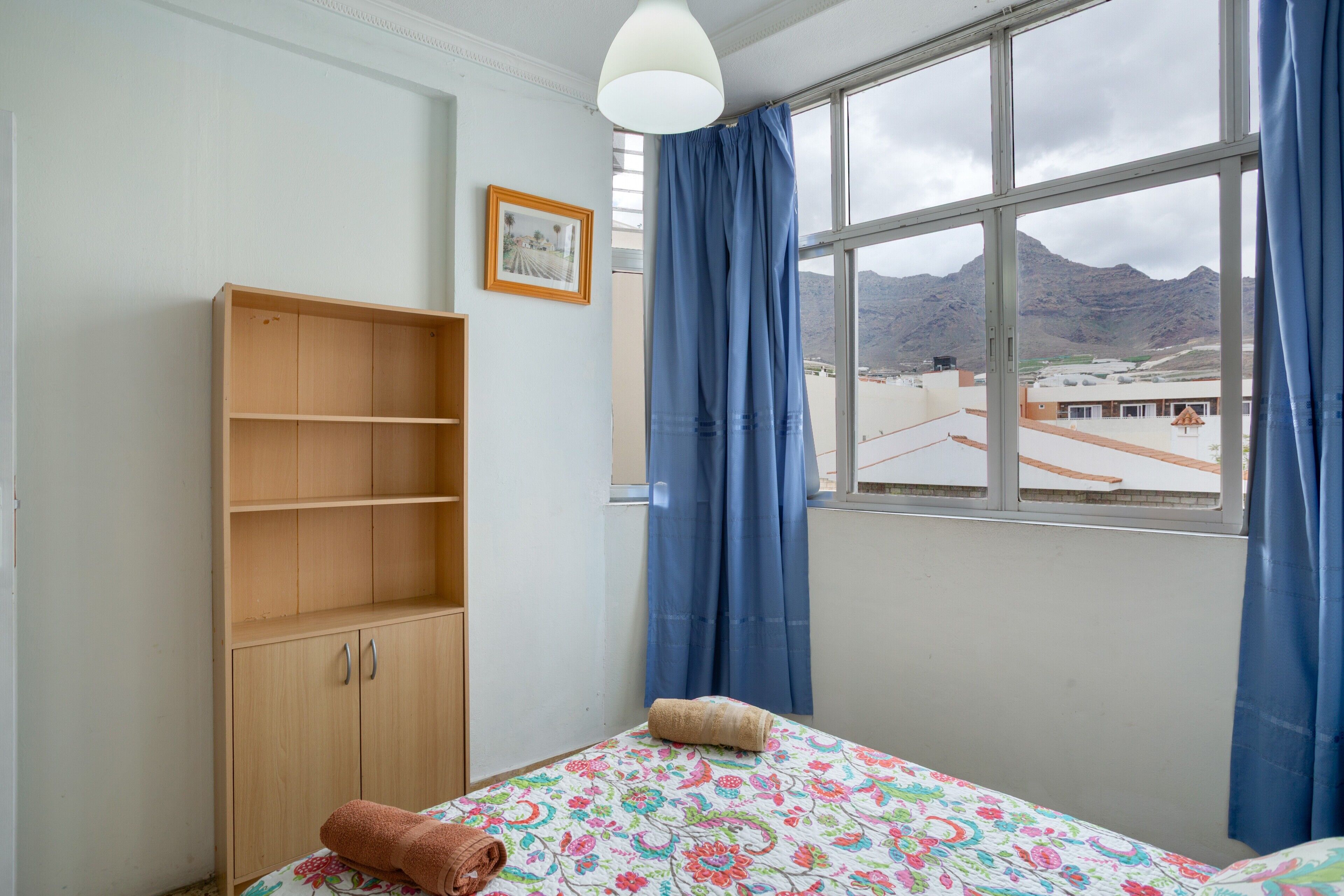 Een slaapkamer met een bed, een houten garderobe, een raam met uitzicht op bergen en een hangende lamp.