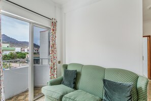 Ein grünes Sofa mit Kissen, ein Balkon mit Blick auf Gebäude und Berge sowie ein gemustertes Vorhang.