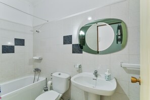 Et badeværelse med badekar, toilet, håndvask og spejl.