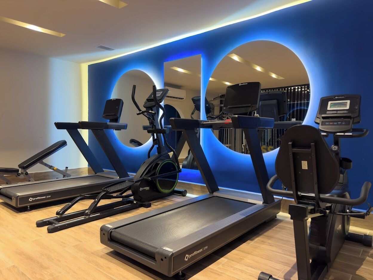 Un gimnasio con cintas de correr, elípticas y una máquina de remo.