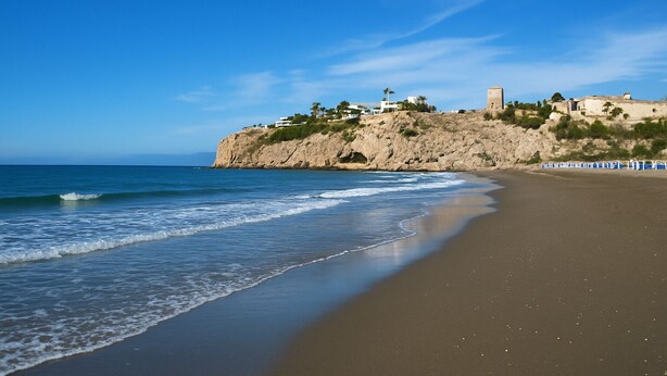 A coastal beach with a rocky cliff, a lighthouse, and buildings on top. - Malaga. Apartamento a un minuto de la playa (Rincón de la Victoria)