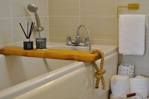 A bathroom with a bathtub, a wooden shelf with candles, a shower head, and a towel rack. - Seaside Nook- stylish stay by the sea (Anstruther)