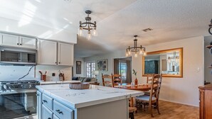 A modern kitchen with a central island, wooden chairs, and a dining table. - Family Friendly Resort | Pool | Yard | Games (Yuma)