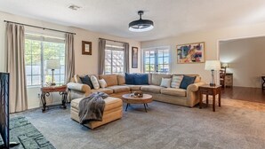 A spacious living room with a large beige sectional sofa, a round coffee table, and a TV on a stand. - Family Friendly Resort | Pool | Yard | Games (Yuma)