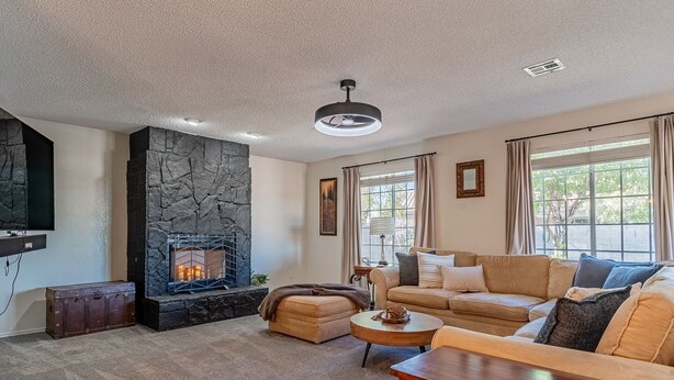 A living room with a stone fireplace, a sofa set, a coffee table, and a TV mounted on the wall. - Family Friendly Resort | Pool | Yard | Games (Yuma)