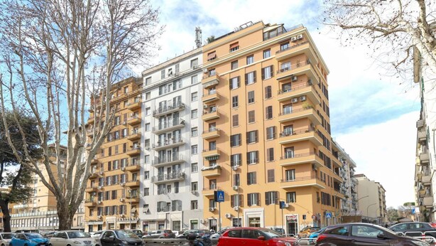 Un edificio residencial de varios pisos con balcones, coches aparcados y árboles.