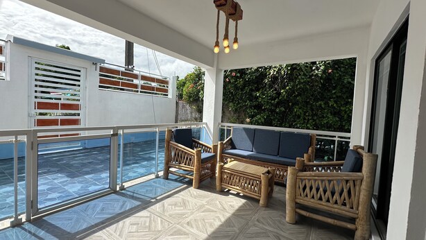 Un espacio al aire libre cubierto con piscina, muebles de madera y una lámpara colgante.