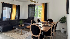 Una sala moderna con un sofá oscuro, una mesa de comedor de madera y sillas, y un ventilador de techo.