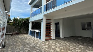 Un edificio moderno de dos pisos con techo plano, ventanas amplias y un espacio exterior cubierto con suelo de piedra estampada.