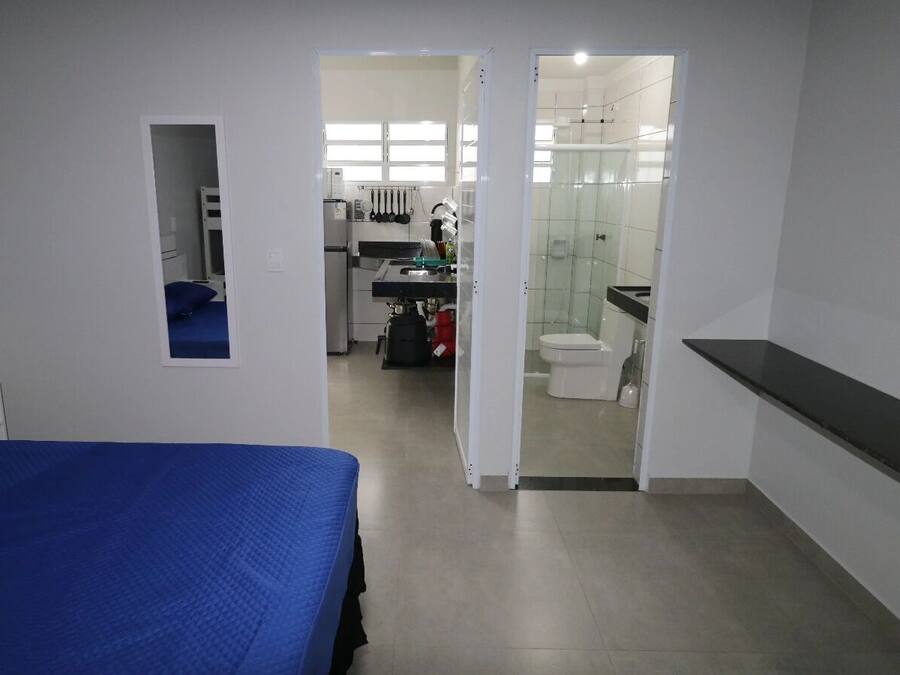 Une chambre avec un lit, une petite table de chevet, un miroir et une vue sur la salle de bain et la cuisine.