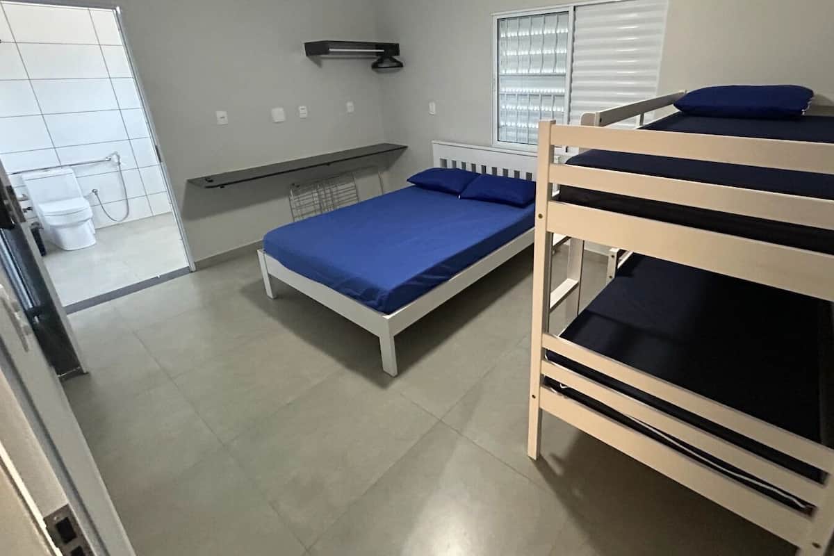 Une chambre de dortoir avec des lits superposés, une fenêtre avec des stores, un radiateur et une petite étagère.