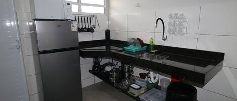 Una cocina compacta con refrigerador, pileta y diversos utensilios de cocina.