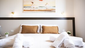 A neatly made bed with white linens and two brown pillows, a painting of two figures on a beach, and a small potted plant on the bedside table. - Easylife - A 2 passi dal mare Sant'Isidoro (Sant'Isidoro)