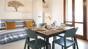 A modern living room with a sofa, dining table, and chairs. There is a painting on the wall and a window with a view. - Easylife - A 2 passi dal mare Sant'Isidoro (Sant'Isidoro)