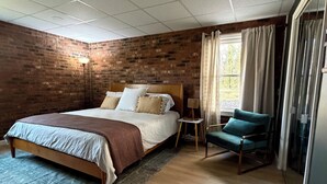 Un dormitorio con cama, una silla, una lámpara y una ventana con cortinas.
