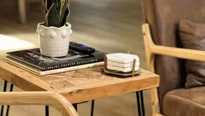 Una mesa de centro de madera con una planta en maceta, un libro titulado 'Carolina County Reflections' y una pila de platos blancos.