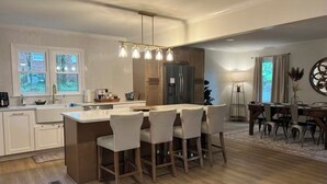 Una cocina moderna con una isla central, taburetes de bar, un refrigerador y un comedor con candelabro.