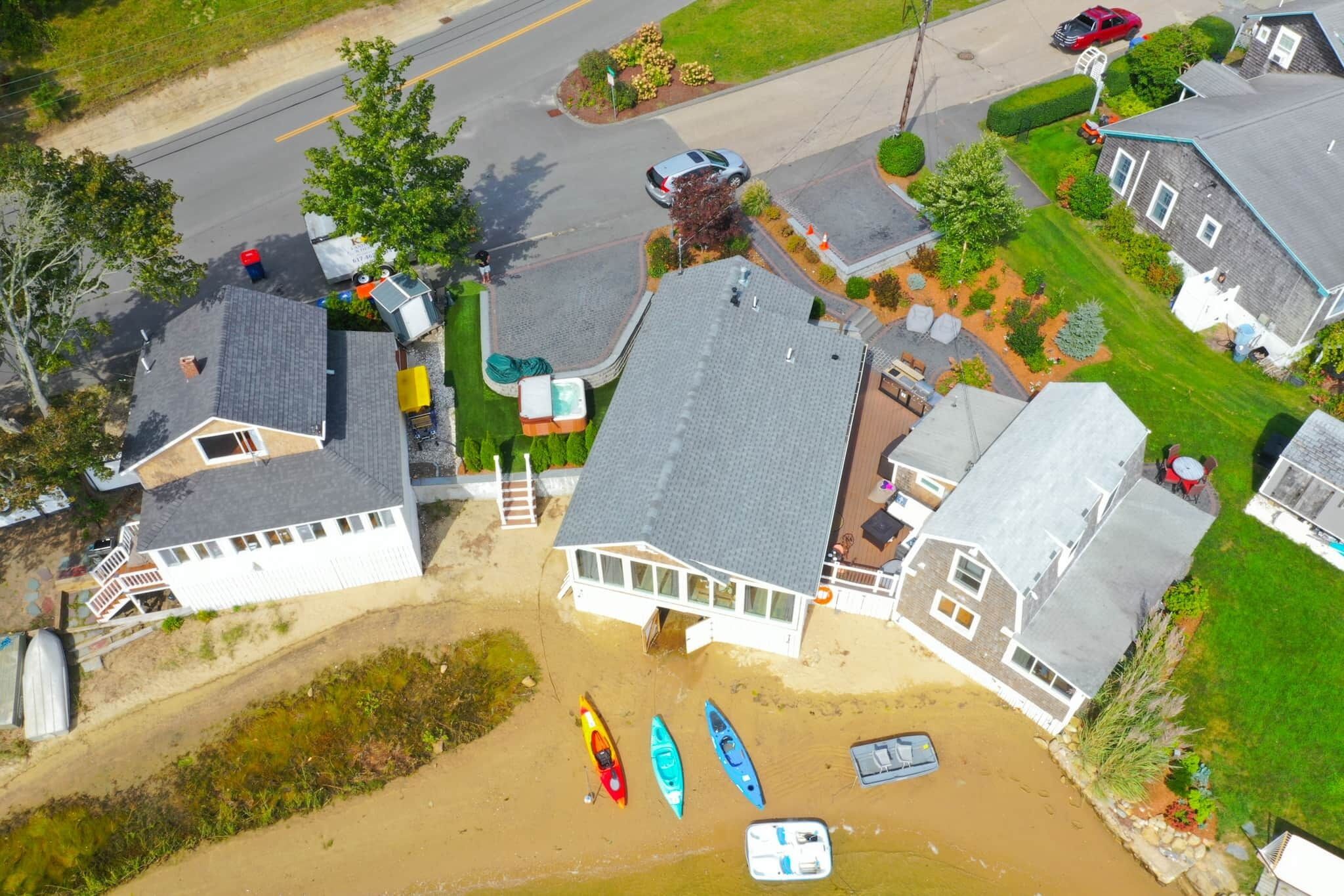 An aerial view of a residential area with houses, a road, and a beach with kayaks.