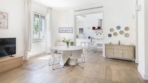 Een moderne woonkamer met een ronde eettafel, een flatscreen televisie en een keuken met kasten en een aanrecht.