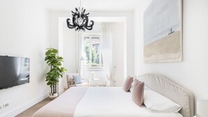 Een moderne slaapkamer met een groot bed, een flatscreen televisie, een potplant en een schilderij aan de muur.