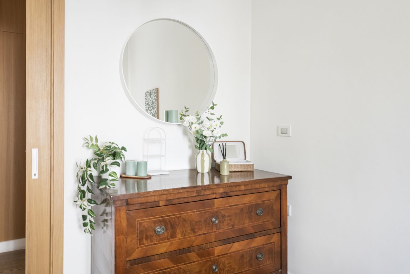 Une commode en bois avec un miroir au-dessus, un vase avec des fleurs et une petite plante placée à côté de la commode.