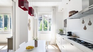 Een moderne keuken met witte kasten, een groot raam en een eethoek met een witte tafel en een schaal citroenen.