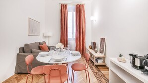 Ein moderner Essbereich mit einem runden Tisch für vier Personen, einer Couch und einer Küchenzeile mit Geräten.