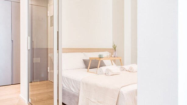 Une chambre à coucher avec un lit, une table de chevet sur laquelle se trouvent une tasse et une plante, et une serviette sur le lit.