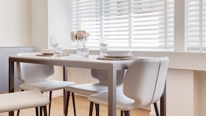 Un coin repas avec une table dressée pour deux personnes, deux chaises et une fenêtre avec des stores.