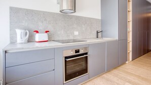 Une cuisine moderne avec des meubles gris, un four encastré, une hotte de cuisinière en acier inoxydable et un plan de travail sur lequel se trouvent une bouilloire et un grille-pain.